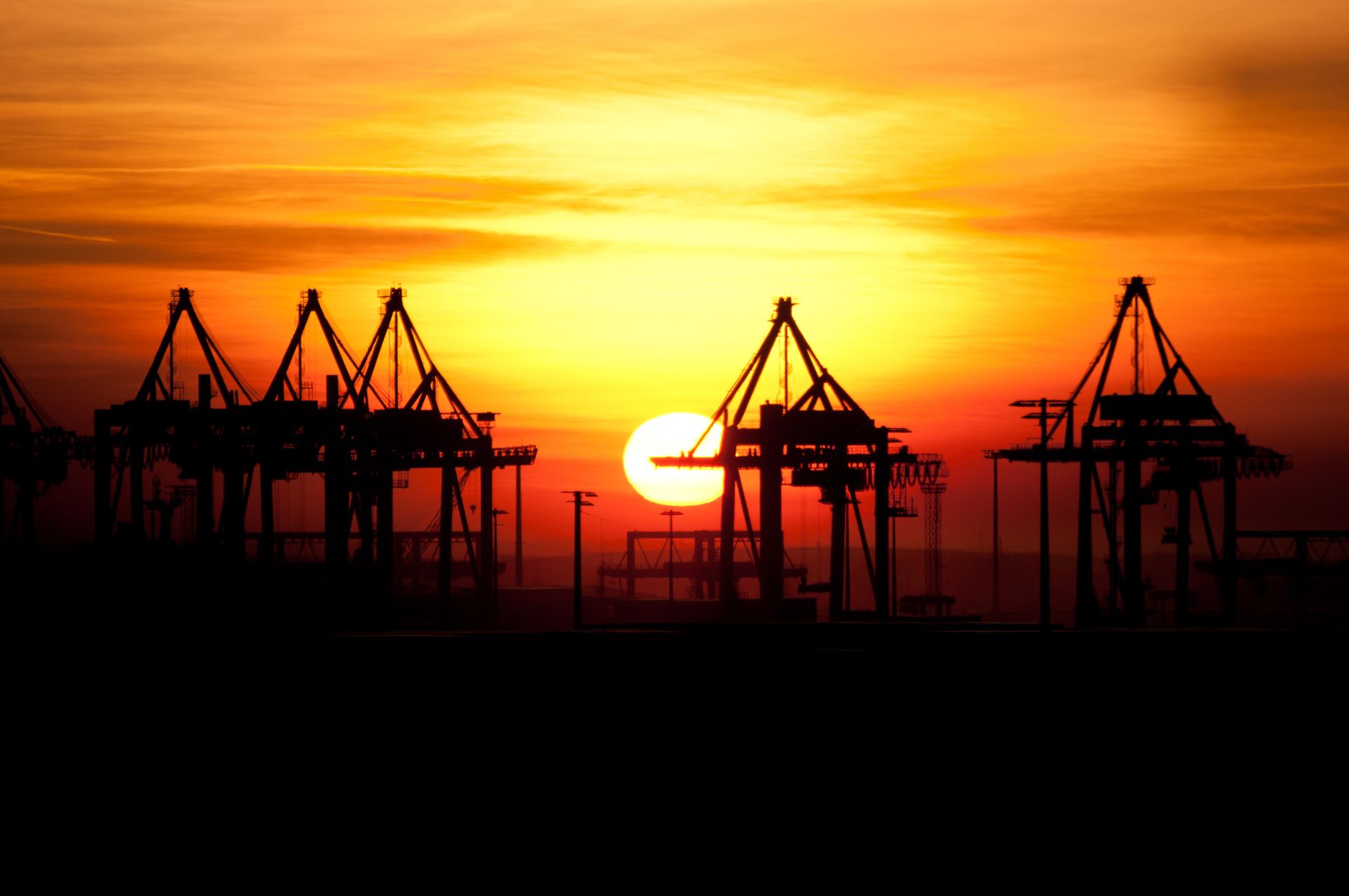 Havnekraner i silhuet mod en solnedgang over havnen